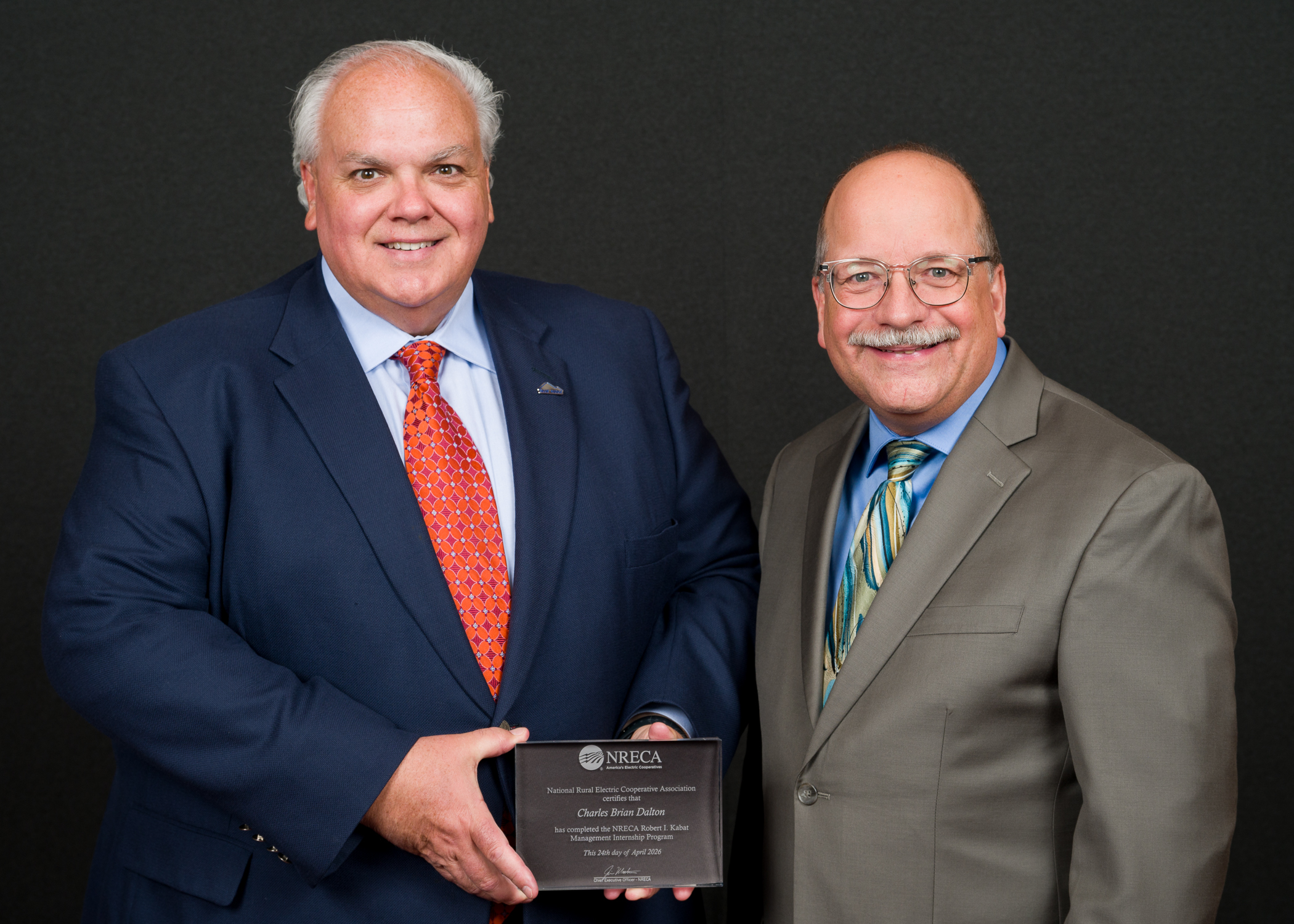Two men pose for a picture together holding an achievement plaque